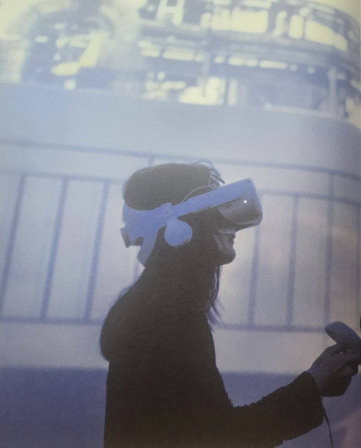 A visitor in a VR headset holding a controller, in silhouette against a projected image.